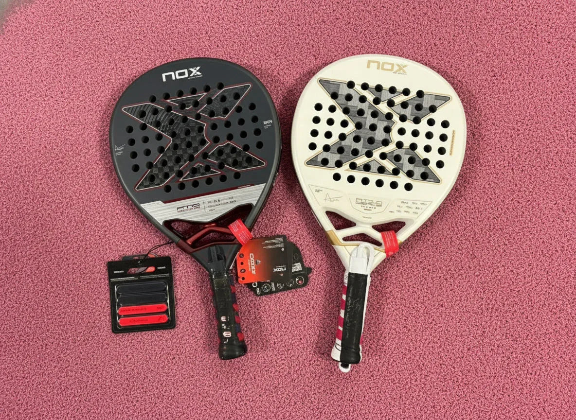 Two NOX padel rackets, one black and one white, on a pink textured surface with accessories