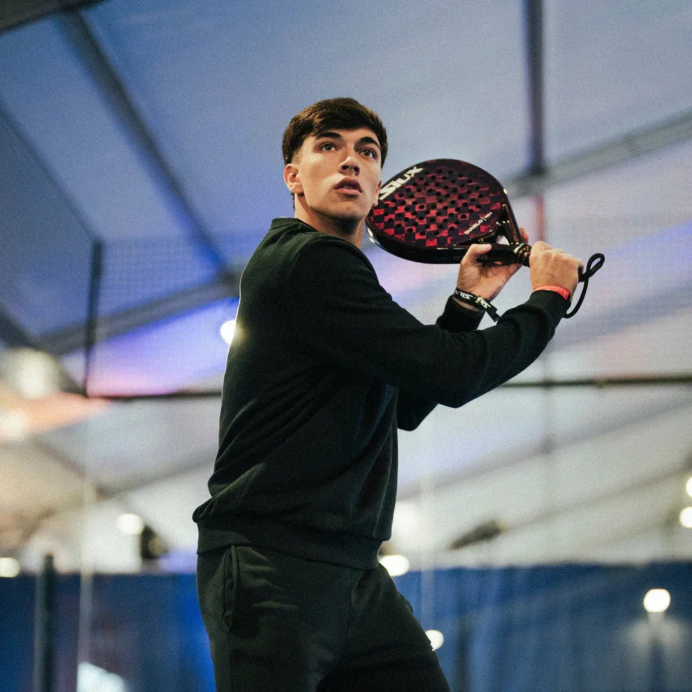 Young man playing padel indoors holding a red and black Siux Diablo paddle