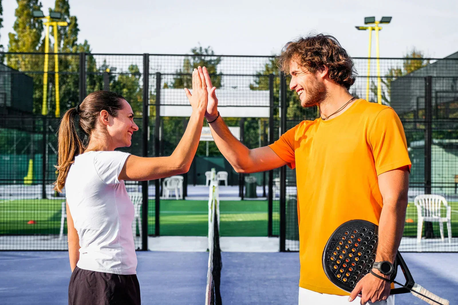 Two padel players giving a high five on an outdoor padel court with rackets and net