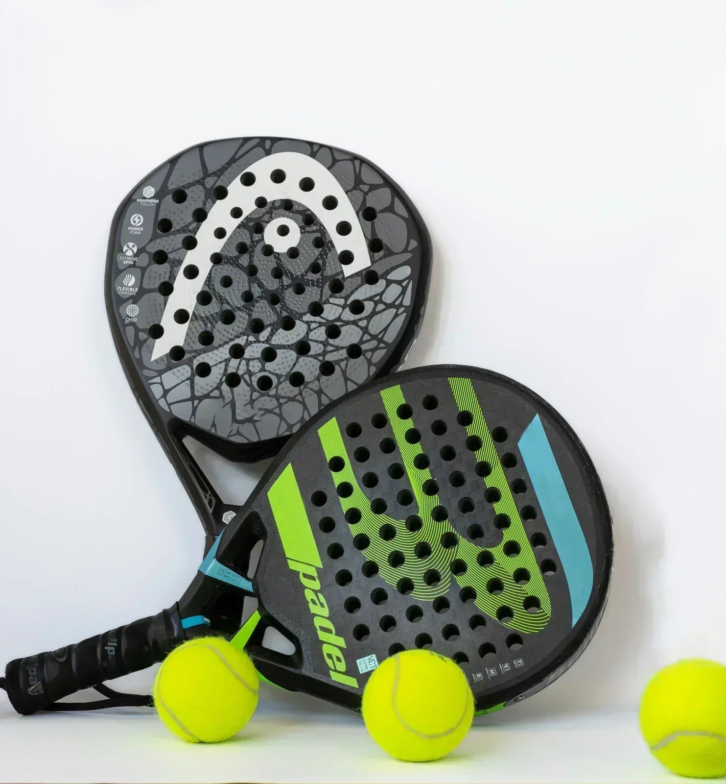 Two black padel rackets with green and white designs alongside three yellow padel balls on white background